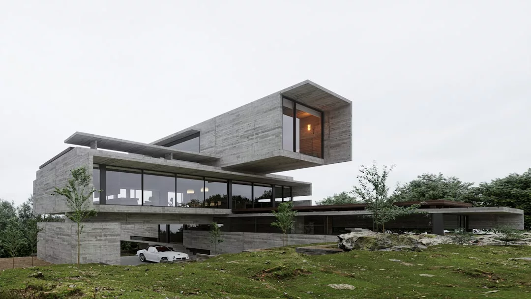 Ein modernes, mehrstöckiges Haus auf Mallorca aus Sichtbeton und Glas mit auskragenden Teilen, großen Fenstern und einem darunter geparkten weißen Auto in einer grasbewachsenen, felsigen Landschaft.