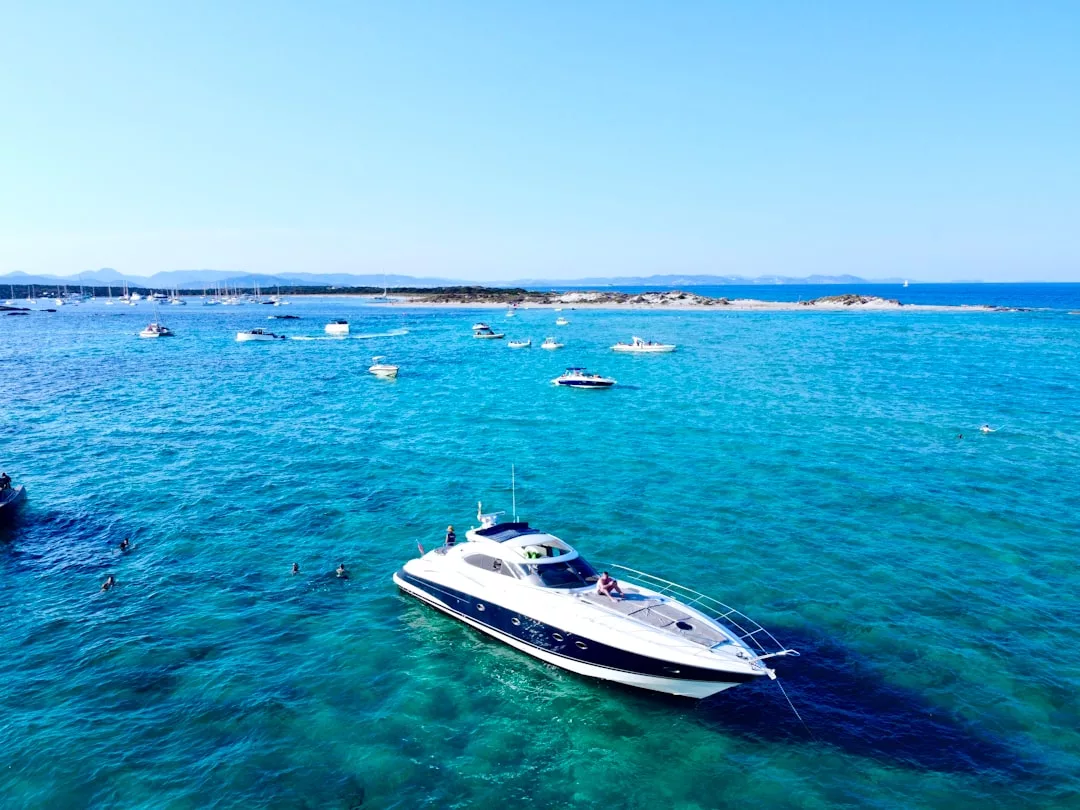 Eine weiß-blaue Motoryacht liegt im klaren blauen Meer vor Mallorca vor Anker, umgeben von mehreren kleineren Booten und weit entferntem Land unter einem klaren Himmel.