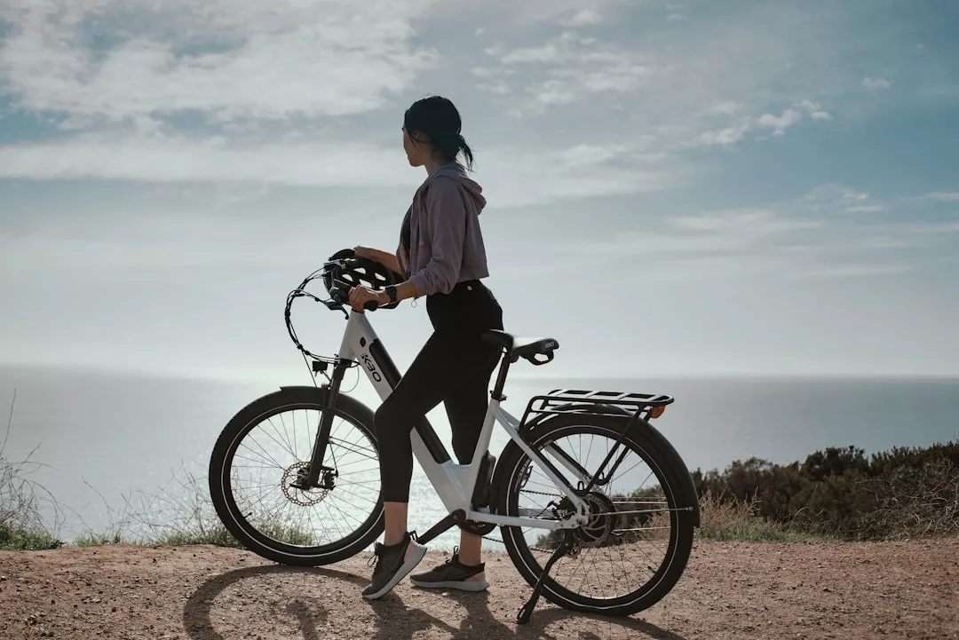 Eine Person steht neben einem Fahrrad auf einem unbefestigten Weg in Mallorca und blickt bei teilweise bewölktem Himmel auf das Meer.