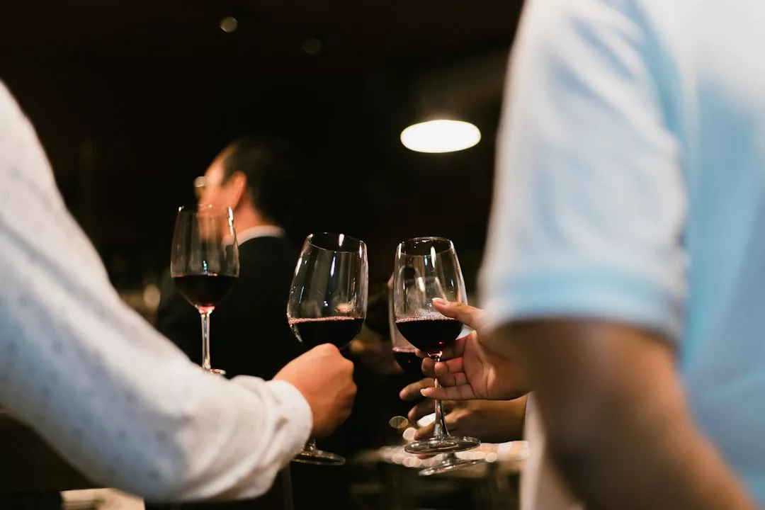 Drei Personen, die bei einem geselligen Beisammensein auf Mallorca Gläser mit Rotwein in der Hand halten und darauf anstoßen, wobei im Hintergrund ein weiterer Gast zu sehen ist.