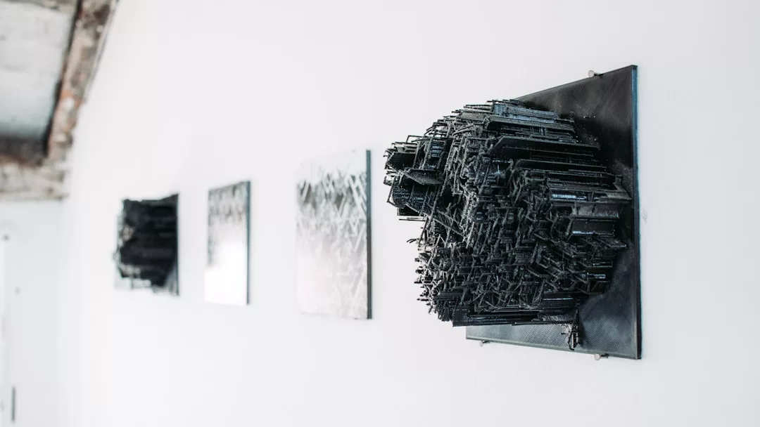Ein schwarzes, geometrisches, dreidimensionales Kunstwerk ist an einer weißen Wand neben zwei flachen, gerahmten Kunstwerken in einer Galerie auf Mallorca angebracht.