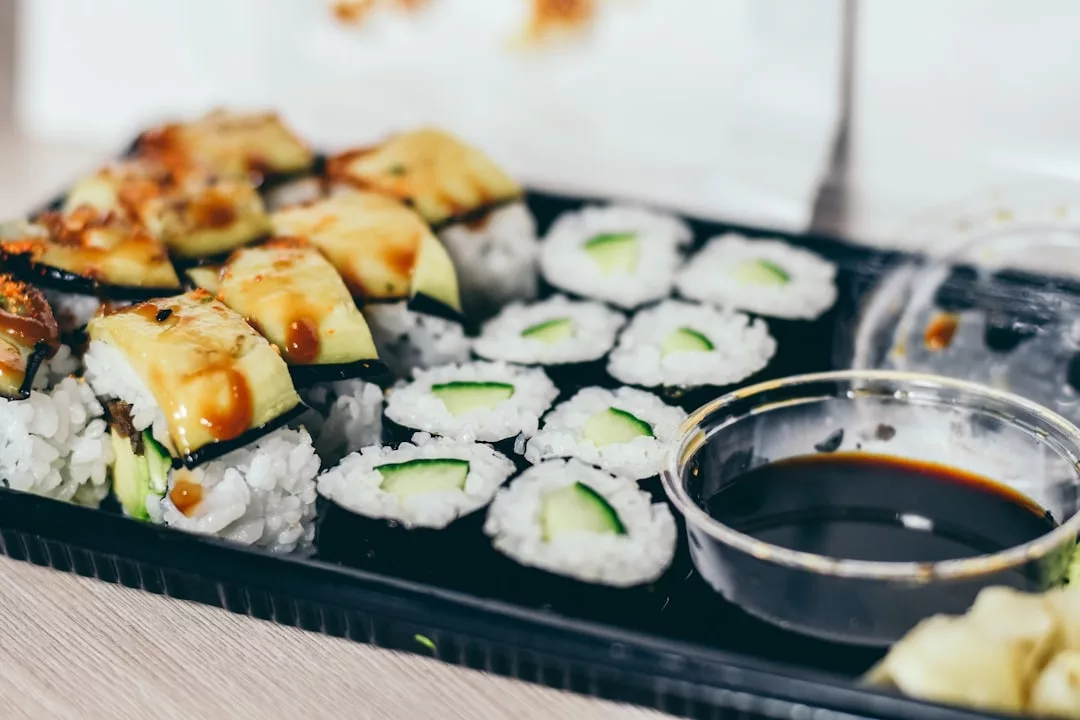 Ein schwarzes Tablett mit verschiedenen Sushi-Rollen, darunter Gurken-Maki und Avocado-Rollen, serviert mit einem Behälter mit Sojasauce - perfekt, um die lebendige Küche Mallorcas zu genießen.