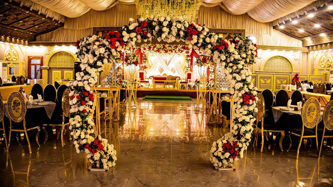 Aufwendig dekorierter Festsaal mit goldenen Akzenten, ein mit weißen und roten Blumen geschmückter Torbogen und eine Bühne mit verzierten Sitzgelegenheiten im Hintergrund, die an die Eleganz Mallorcas erinnern.