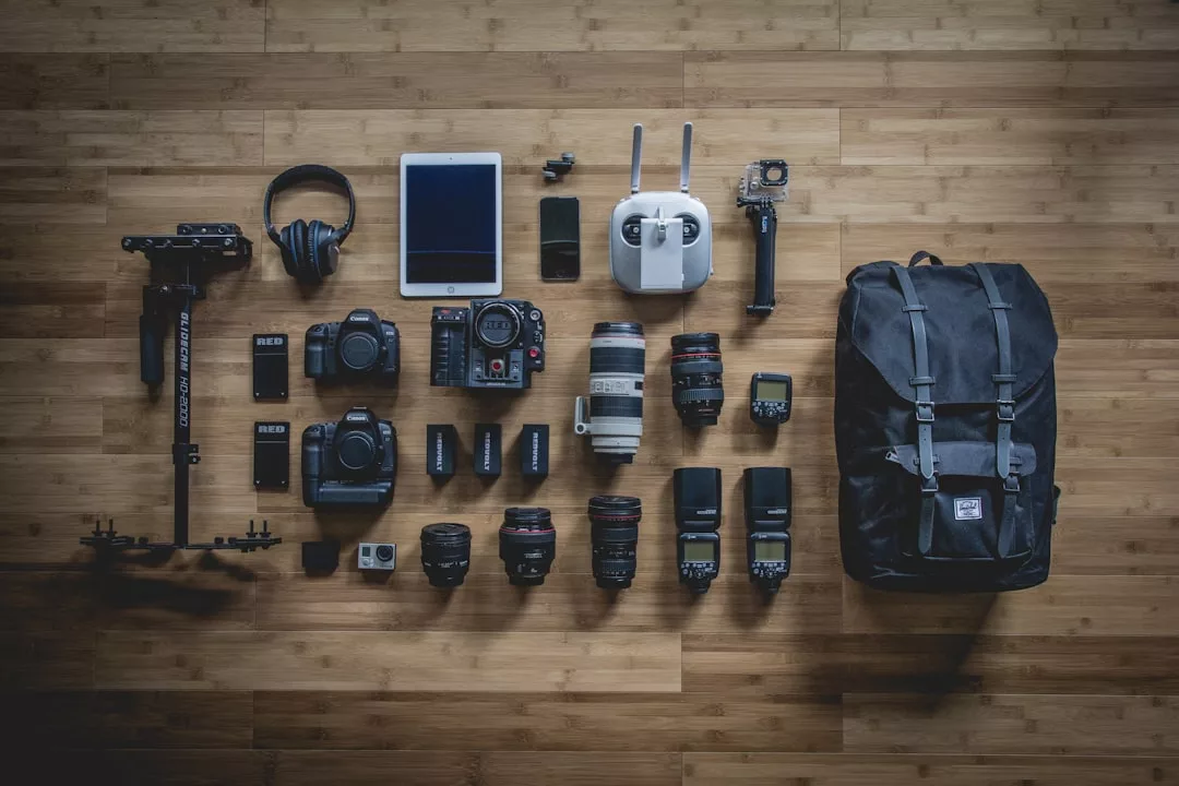 Die Foto- und Videoausrüstung liegt fein säuberlich auf dem Holzboden, darunter Kameras, Objektive, ein Drohnen-Controller, Kopfhörer, ein iPad, Action-Kameras und ein schwarzer Rucksack - die perfekte Ausrüstung, um die atemberaubende Landschaft Mallorcas einzufangen.