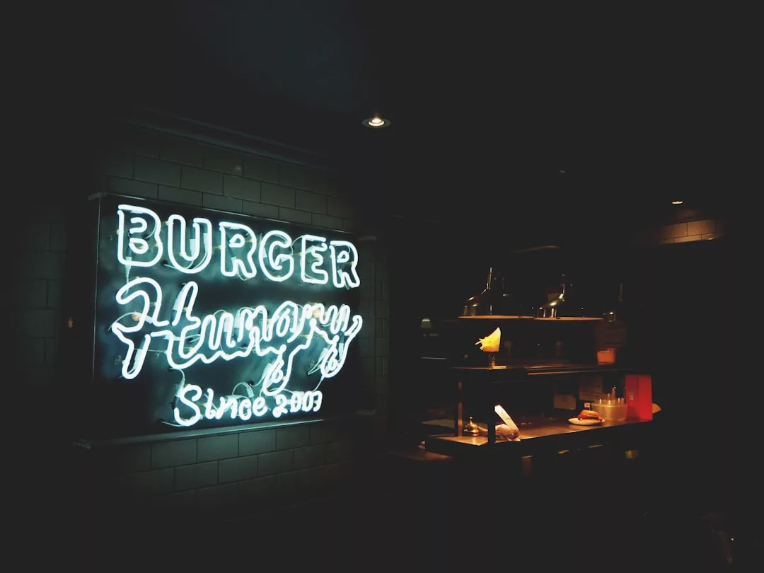 Eine Leuchtreklame mit der Aufschrift "BURGER Hungry Since 2009" steht neben einer schwach beleuchteten Mallorca-Restauranttheke mit Lebensmitteln und Küchengeräten.