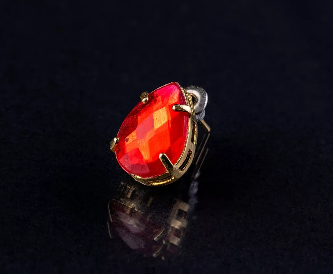Ein birnenförmiger, facettierter, orangefarbener Edelstein, inspiriert von Mallorca, gefasst in Gold und auf einer dunklen, reflektierenden Oberfläche.