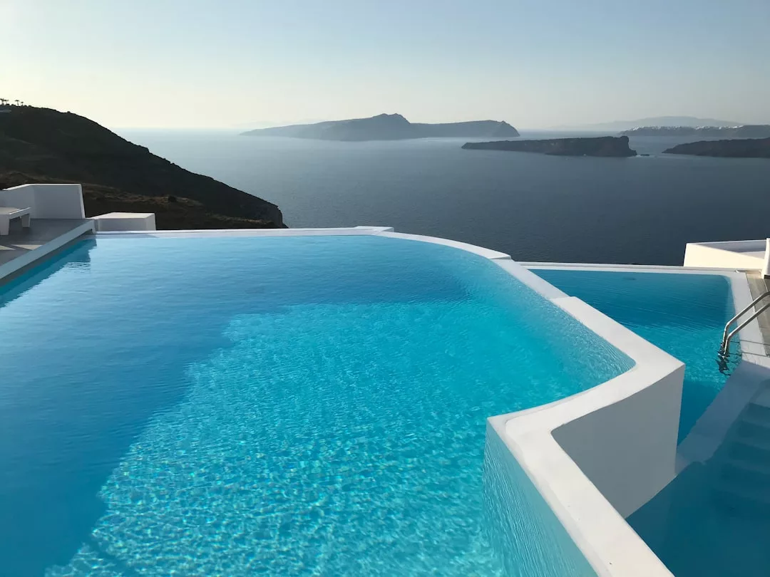 Ein Infinity-Pool mit klarem, blauem Wasser und Blick auf das Meer und die fernen Inseln unter einem klaren Himmel, umrahmt von weißer, moderner Architektur - eine idyllische Flucht, inspiriert von Mallorcas zeitloser Schönheit.