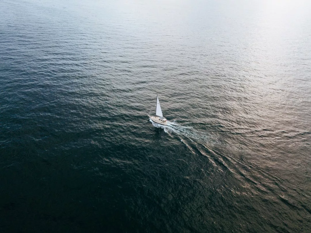 Ein einzelnes Segelboot mit weißem Segel gleitet über die ruhigen, offenen Gewässer Mallorcas und hinterlässt sanfte Wellen unter einem bedeckten Himmel.