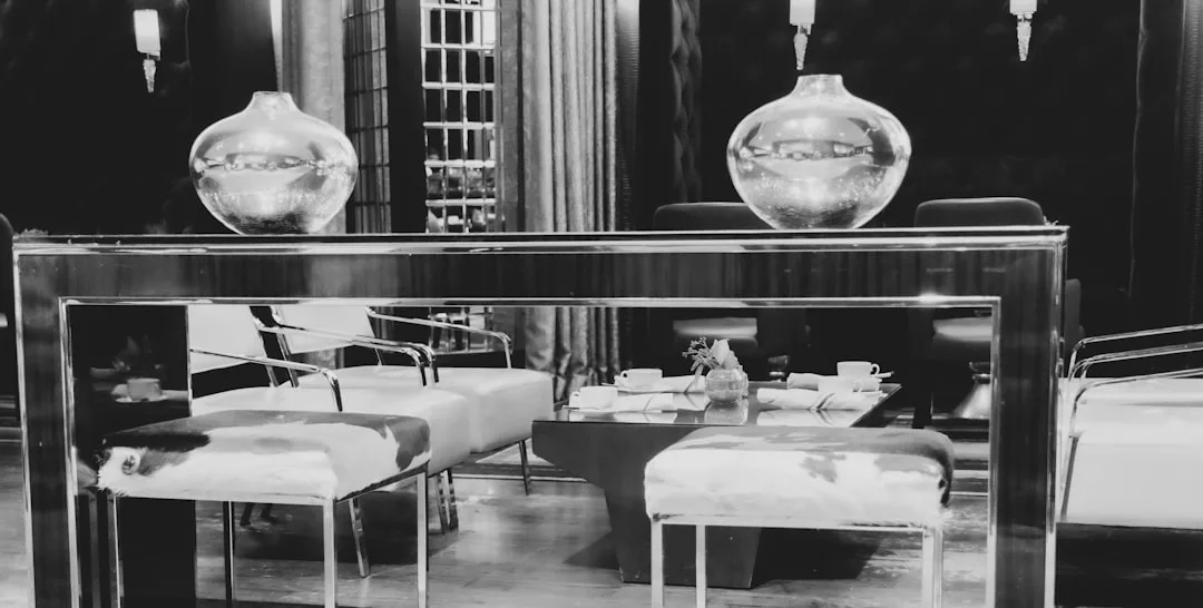 Schwarz-Weiß-Foto einer modernen Mallorca-Lounge mit Sesseln, einem Glastisch mit Teetassen und zwei dekorativen Vasen auf einer verspiegelten Konsole.
