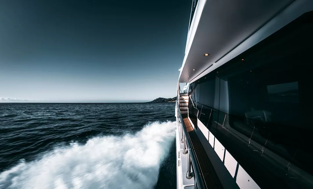 Blick vom Seitendeck einer fahrenden Yacht in der Nähe von Mallorca auf das Meer, die weißen Wellen und das ferne Land unter einem klaren Himmel.